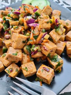 a black plate topped with tofu and veggies