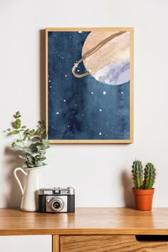 a painting hanging on the wall above a wooden table with a camera and potted plant