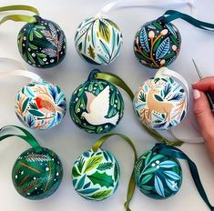 hand painted christmas ornaments are being decorated with green ribbon and scissors on a white surface