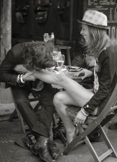 two people sitting at a table with wine glasses in their hands and one person holding the other's head