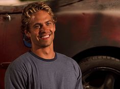 a man standing in front of a red truck smiling at the camera with his hands on his hips