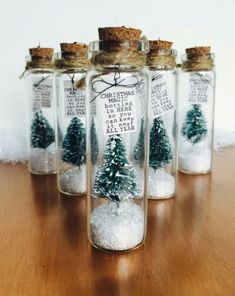 four glass bottles filled with snow and small pine trees in them on top of a wooden table