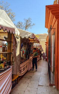 a man walking down a street next to a store filled with goods and people looking at items