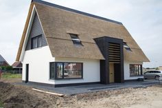 a white house with a thatched roof and black trim on the windows, next to a car parked in front of it