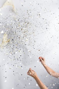 two hands reaching for confetti on a white background with gold and silver sprinkles