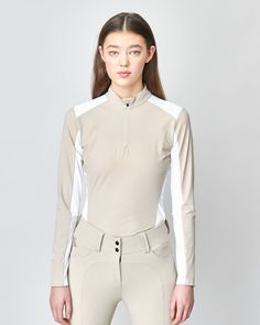 a woman is standing in front of a white wall wearing a beige and white equestrian outfit