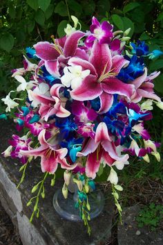 a bouquet of flowers sitting on top of a stone bench next to trees and bushes