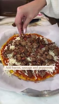 a person placing toppings on top of a homemade pizza pie with cheese and meat