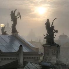 two statues on top of a building with the sun in the background