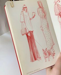 a hand holding an open book with drawings of women in dresses and purses on it