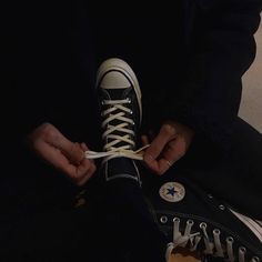 someone tying their shoes with white laces on the bottom and black converse high top sneakers