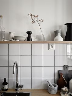 a kitchen with white tile and black accessories on the counter top, including vases