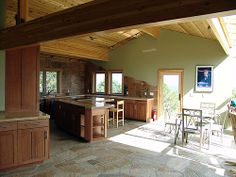 an open kitchen and dining room area with stone flooring, wood beams and ceiling