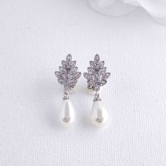 pair of white pearl and cubicge earrings with crystal leaves on the top, in front of