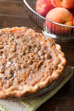 a pie sitting on top of a wooden table next to a bowl of apples in the background