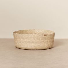 a large round basket sitting on top of a table next to a white wall and floor