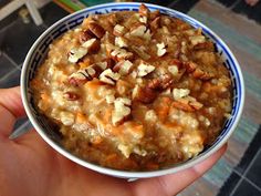 a hand holding a bowl of oatmeal with nuts and cheese on top