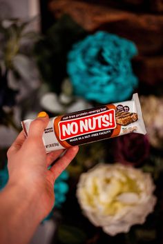 a hand holding a candy bar with no nuts on it in front of some flowers