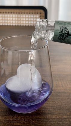 someone is pouring water into a glass with ice cubes in it on a wooden table