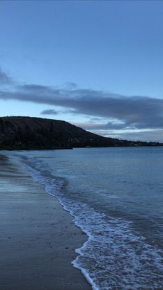 a beach with waves coming in to the shore and hills in the distance at dusk