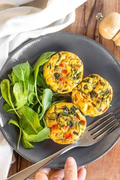 two muffins on a plate with spinach leaves and a fork next to it