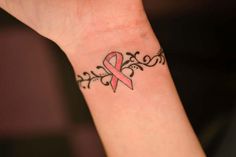 a woman's wrist tattoo with a pink ribbon on it and an ornamental design