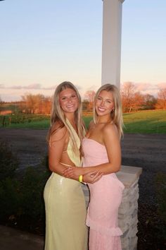 two beautiful women standing next to each other near a pillar in front of a field