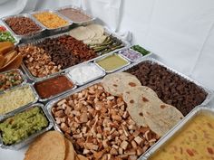 an assortment of different types of food in trays on a table with white cloth