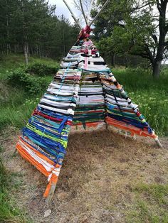 a large pile of books sitting on top of a grass covered field next to trees