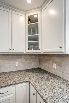 a kitchen with white cabinets and granite counter tops in the center, along with an open cabinet door