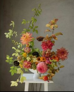 a vase filled with lots of colorful flowers on top of a white table next to a gray wall