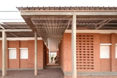 two people are walking down an open walkway in front of a brick building with pergolated roof