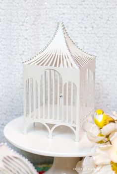 a small white birdcage sitting on top of a cake plate next to flowers