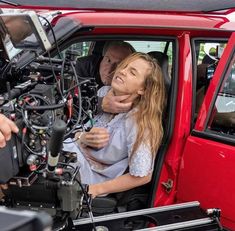 a woman sitting in the driver's seat of a red truck with a man standing next to her