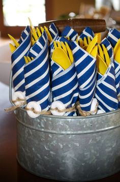 blue and white striped napkins are in a metal bucket with spoons on top