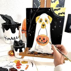 a person is painting a dog in a ghost costume with pumpkins on the table