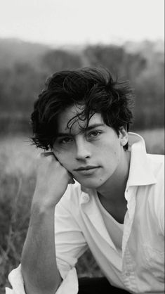 black and white photograph of a young man sitting in a field with his hands on his head