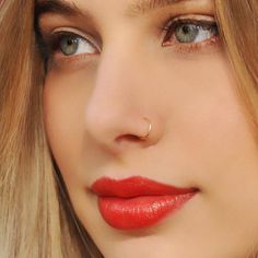 a woman with long blonde hair and blue eyes has a nose piercing on her nose