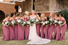 a group of women standing next to each other in front of a brick building holding bouquets