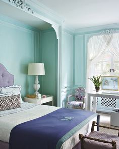 a bed room with a neatly made bed next to a window and a lamp on a table