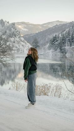 a woman standing in the snow looking out over a mountain lake with mountains in the background