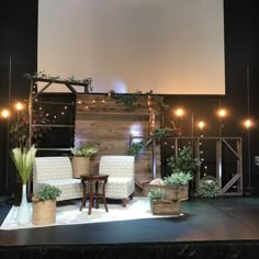 the stage is set up for an event with white chairs and potted plants on it