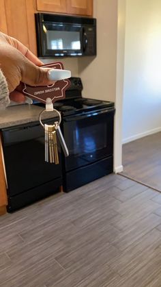 a person holding a house key in front of a kitchen with black stove and microwave