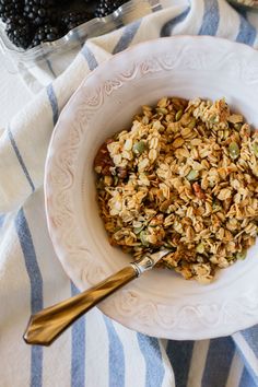 a white bowl filled with granola next to blackberries on a blue and white table cloth