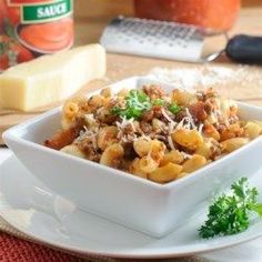 a white bowl filled with pasta on top of a table next to cheese and parmesan