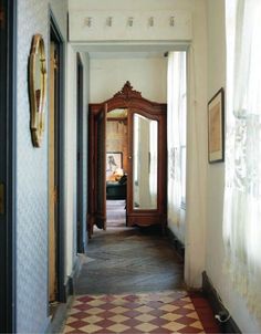 an empty hallway leading to another room with a mirror on the wall and paintings on the walls