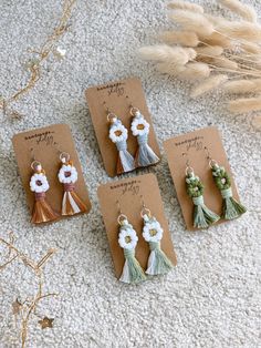 four earrings with flowers and tassels hanging from them on top of a card