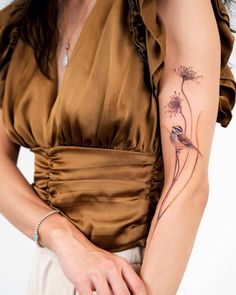 a woman with a tattoo on her arm holding a flower in her left hand and wearing a brown dress