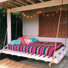 a bed that is sitting on a porch with string lights hanging from the ceiling above it