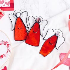 three red angel ornaments sitting on top of a table next to a heart shaped plate